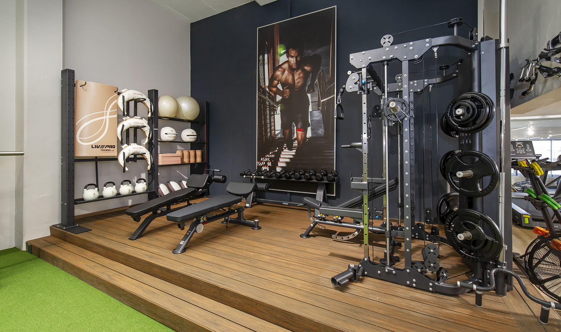 A modern Express Fitness showroom in South Africa, displaying premium gym equipment on a raised wooden platform and artificial turf. The space includes a multi-functional cable machine, adjustable workout benches, and a rack with kettlebells and medicine balls.